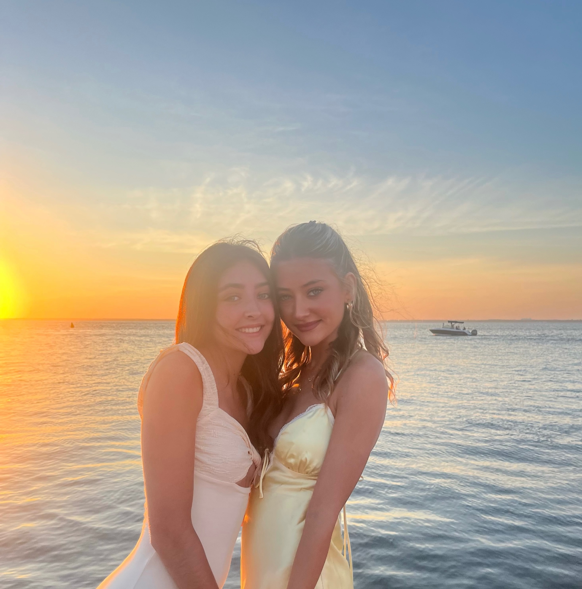 Bernadette's two daughters standing arm in arm by the water at sunset